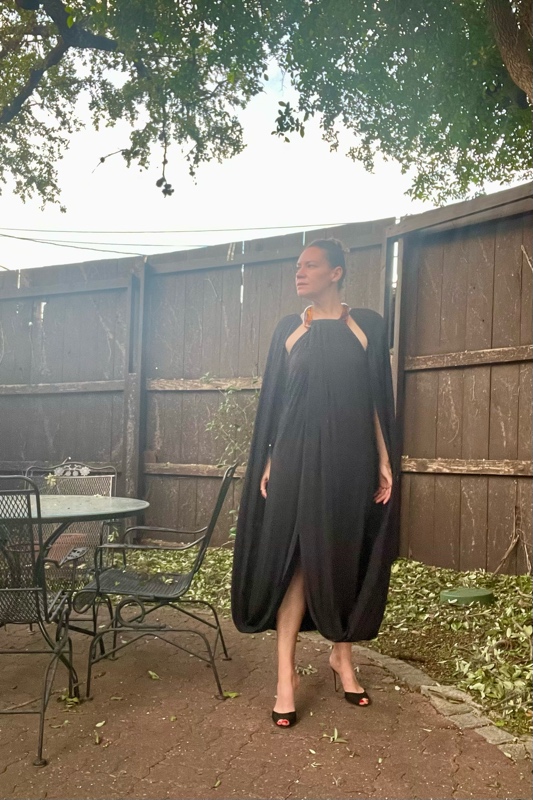  a woman with a black cape dress with a tortoise collar and black heels