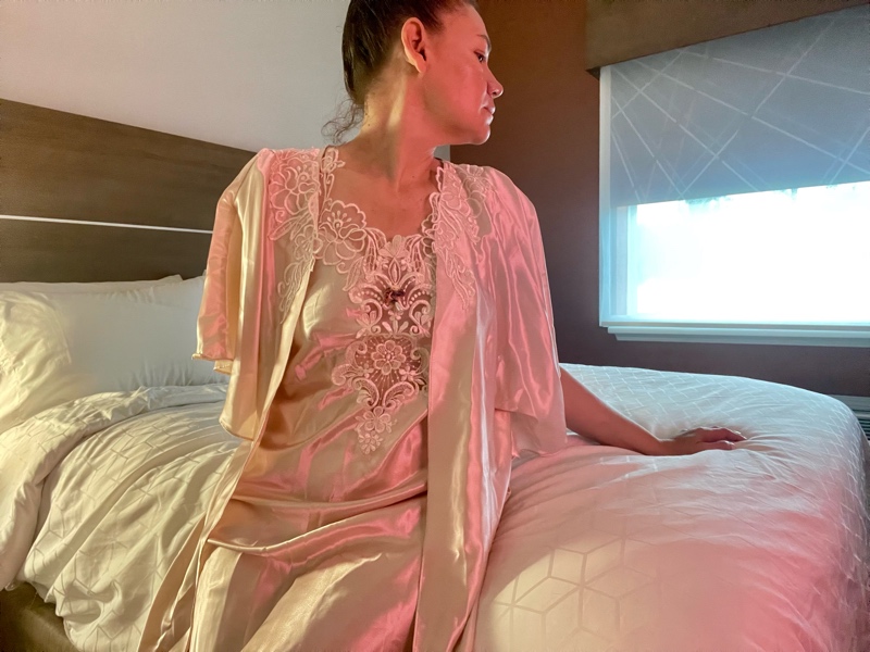 a woman in a pink peignoir set on white bed