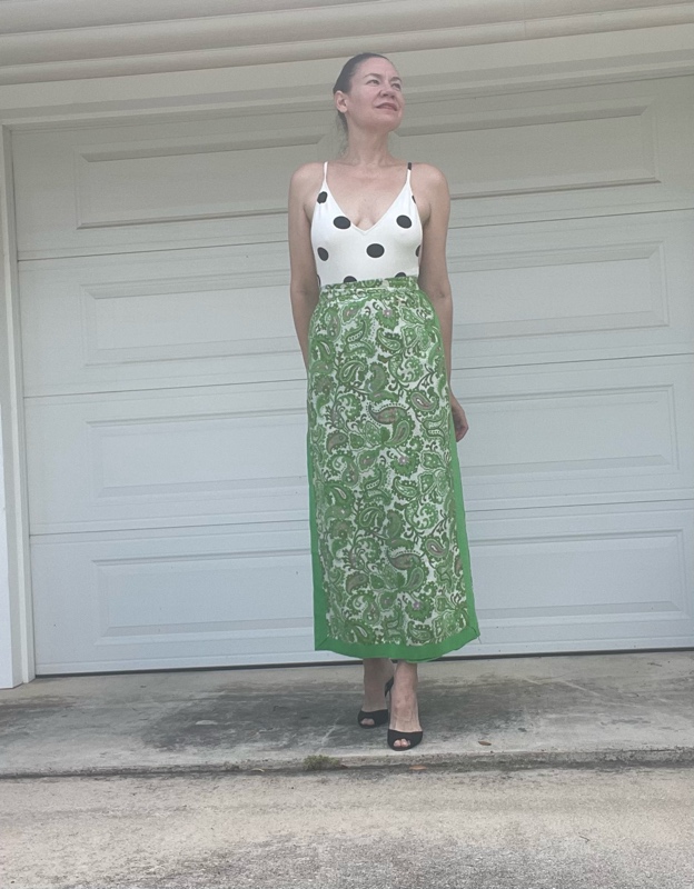 a woman in a white with black polka dot s body suit and a green with embroidered panels maxi skirt and black heeled mules 