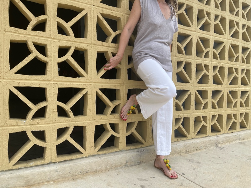 a woman in  white jeans and a sweater vest and raffia sandals 