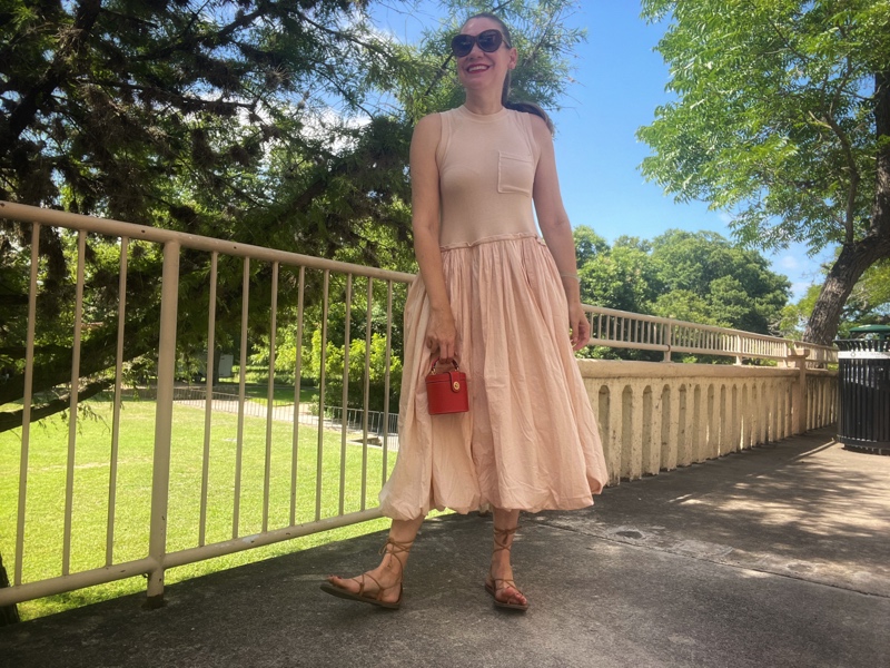 a woman in a beige bubble hem dress, lace up sandals and a red cone clutch