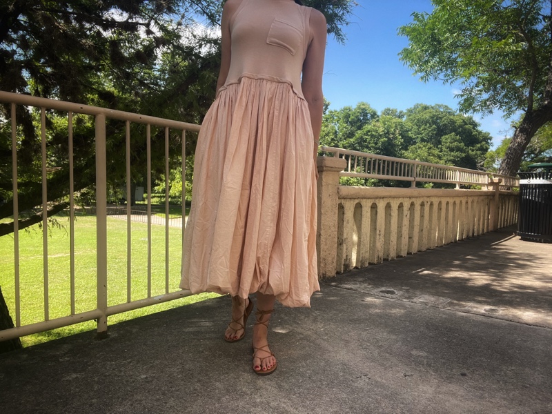 a woman in beige bubble skirt hem dress with lace up sandals and a red circle clutch