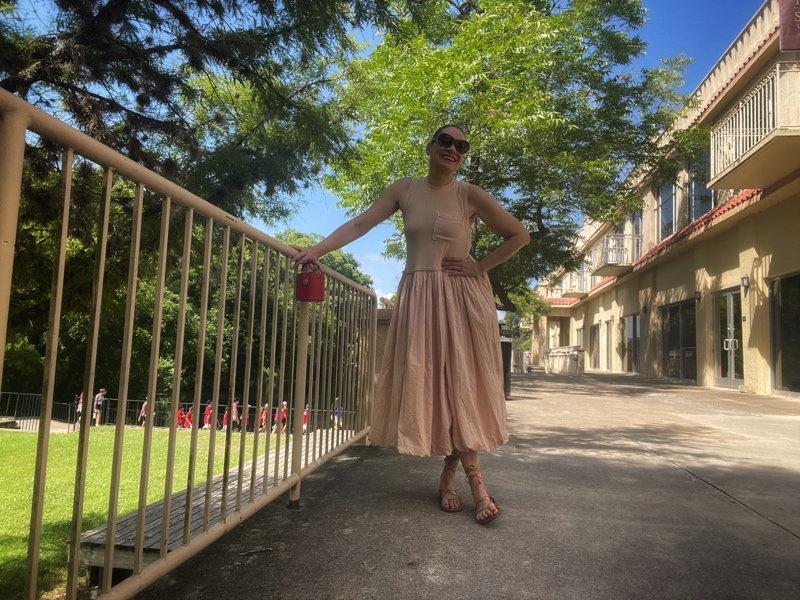a woman in a beige hem bubble dress with lace up sandals and a red cone clutch
