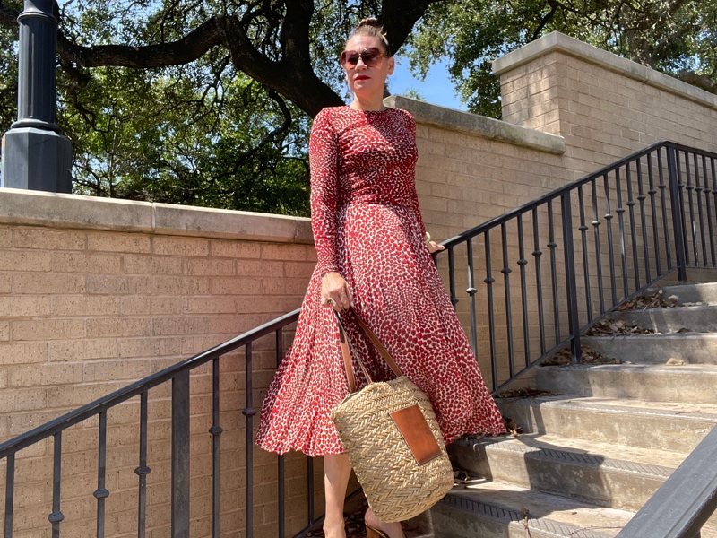 a woman in a strawberry topi and skirt set with a straw and leather tote and gold mules 